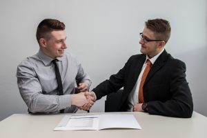 2 businessmen at a table shaking hands