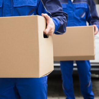 Two men in blue work suits carrying cardboard boxes