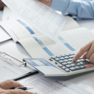 A closeup image of papers, folders and a calculator at a busy office meeting table