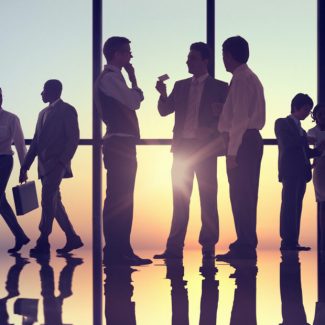 Silhouettes of men negotiated in a office common area with the sunset coming through the glass wall in the background