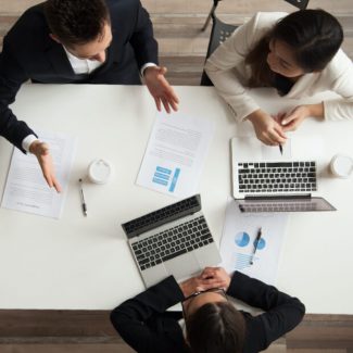 Three business workers discussing lease terms at a meeting table with papers and laptops in hand