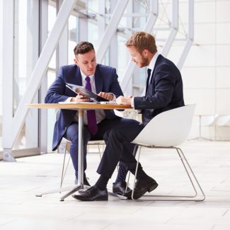 Two men discuss business at a small round table in an office common area