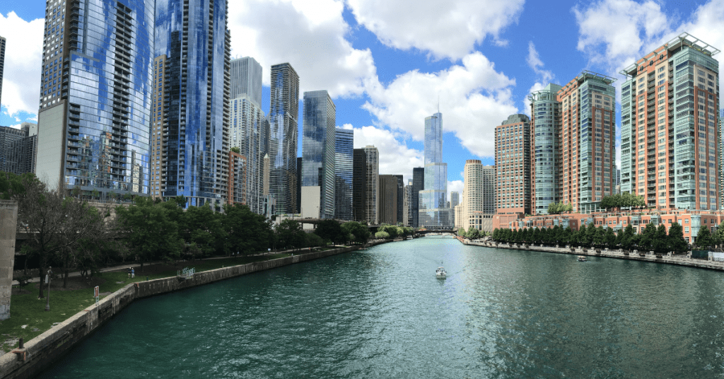 View of a city skyline with skyscrapers along a river under a partly cloudy sky.