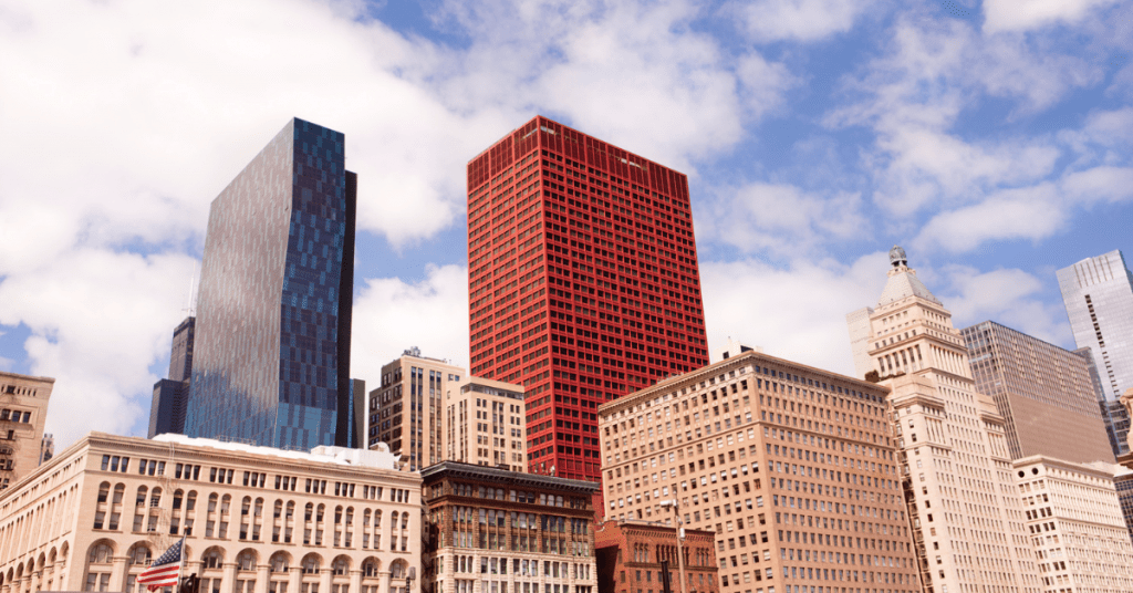 Red skyscraper among other buildings under a partly cloudy sky.