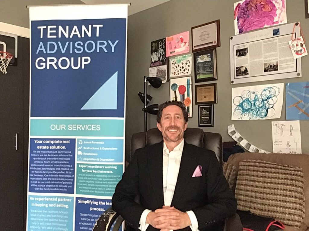 Man in a suit sitting in front of a Tenant Advisory Group display.