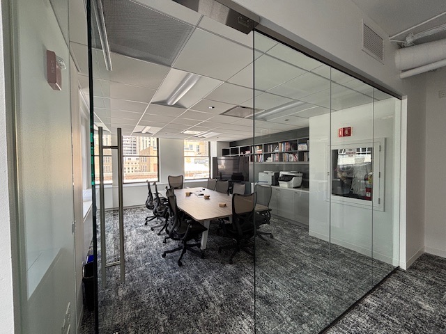 Glass-walled conference room seating eight, with built-in shelving and a city view