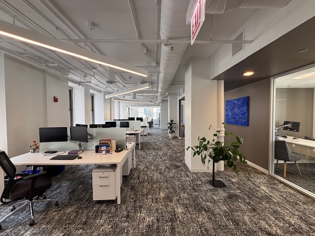 Second open work area with benching desks and a glass-fronted private office