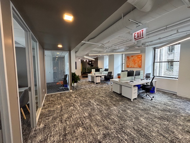 Open-plan workstations beside the window line, with glass-walled offices along the corridor