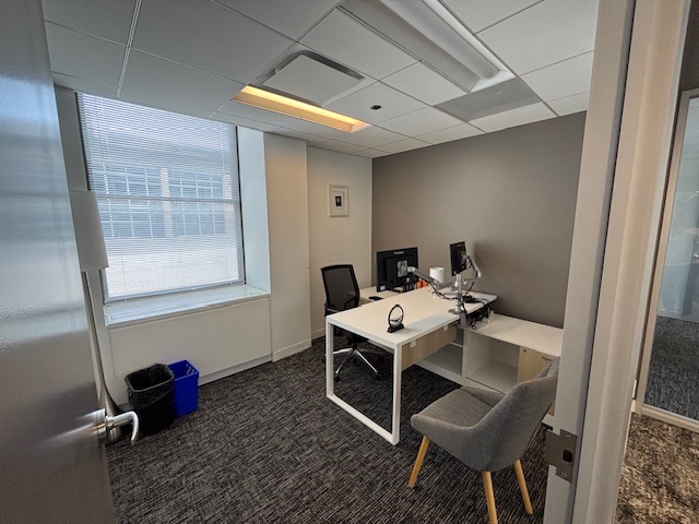 Private office with a desk, guest chair and a window onto the light court