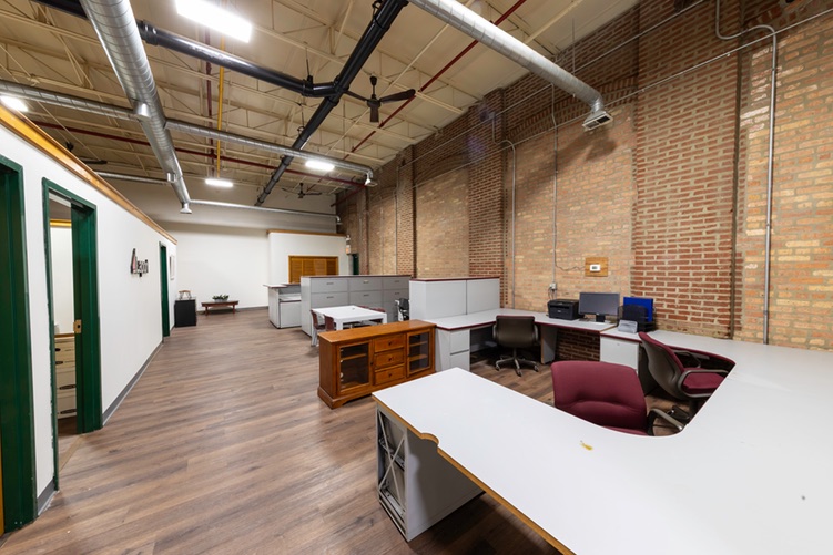 Office workstations against an exposed brick wall beneath an open ceiling