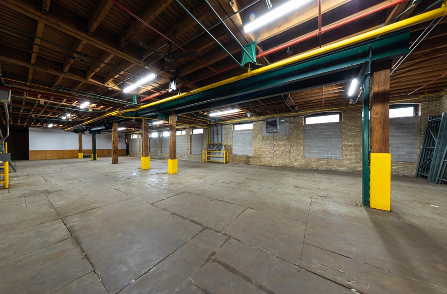 Warehouse floor lit by clerestory windows, with pallet racking stacked at the far wall