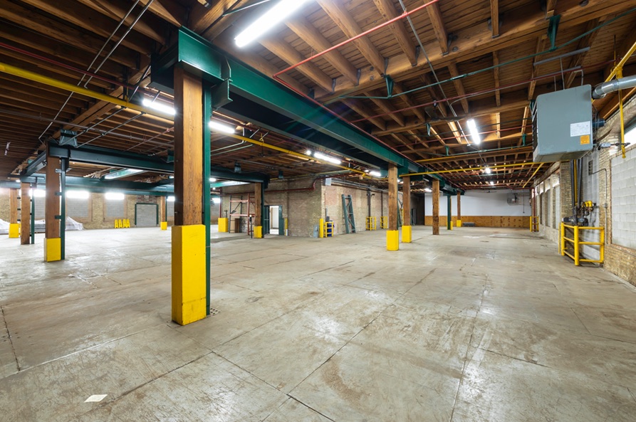 Open warehouse bay with yellow-painted structural columns and strip lighting overhead