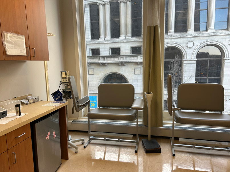Vitals and blood-draw station with two treatment chairs beside the window