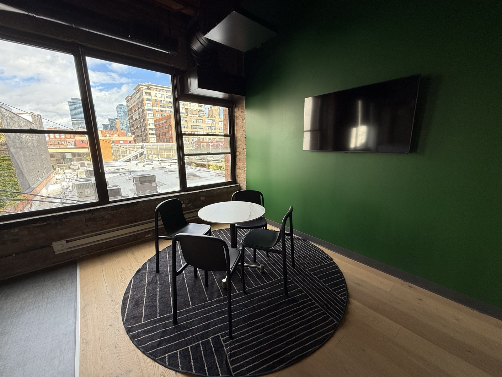 Huddle room with a round table for four, a wall-mounted screen and a city view