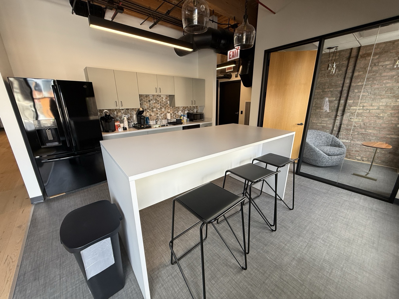 Kitchen with a quartz island, bar stools and a glass-walled phone room alongside